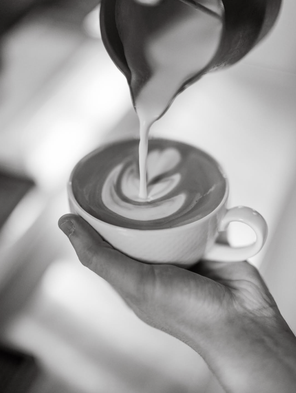 Barista pouring steamed milk into a latte with heart-shaped art at 1824
