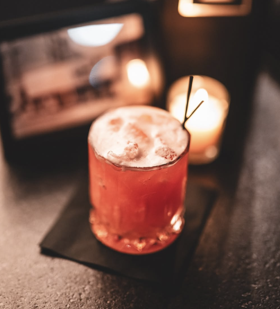 Red rocks cocktail with foam in a faceted glass beside flickering candles